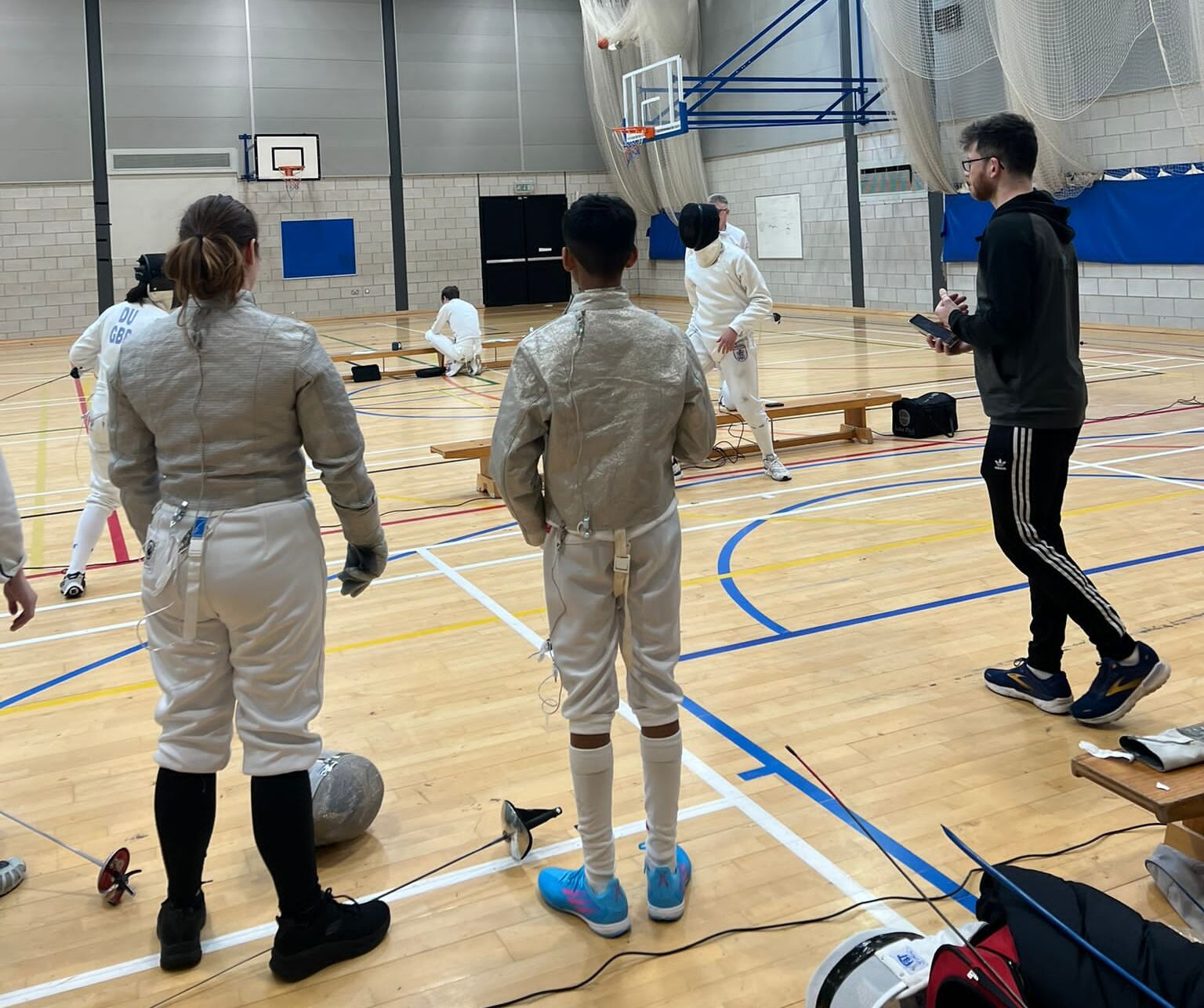 a group of fencers watching sparring in a sports hall