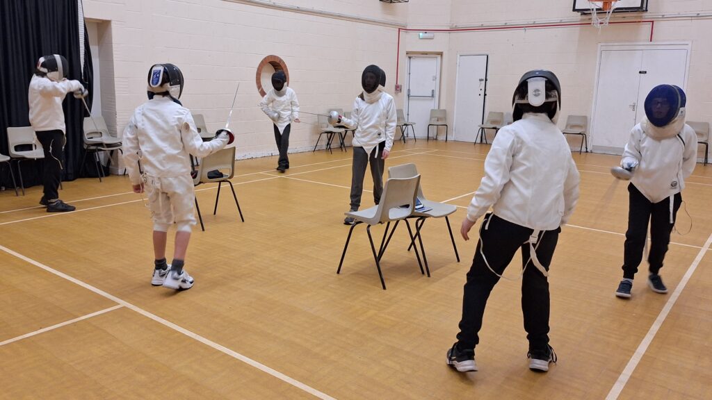 a group of young fencers in a sports hall sparring using electrical scoring equipment.